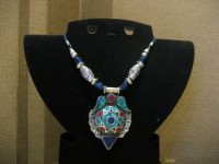 Colgante tibetano en color plateado con incrustaciones de piedra en tonos turquesa y rojo.